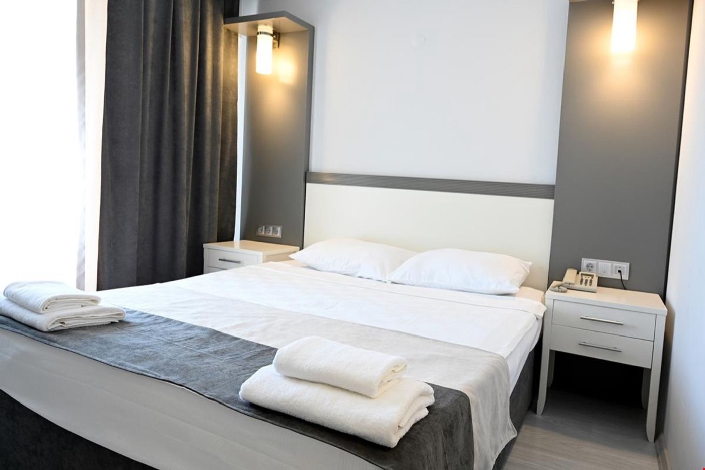 Çift kişilik yatak, havlular ve komodinlerle sade otel odası